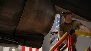 Airman stand behind engine with American Flag behind him