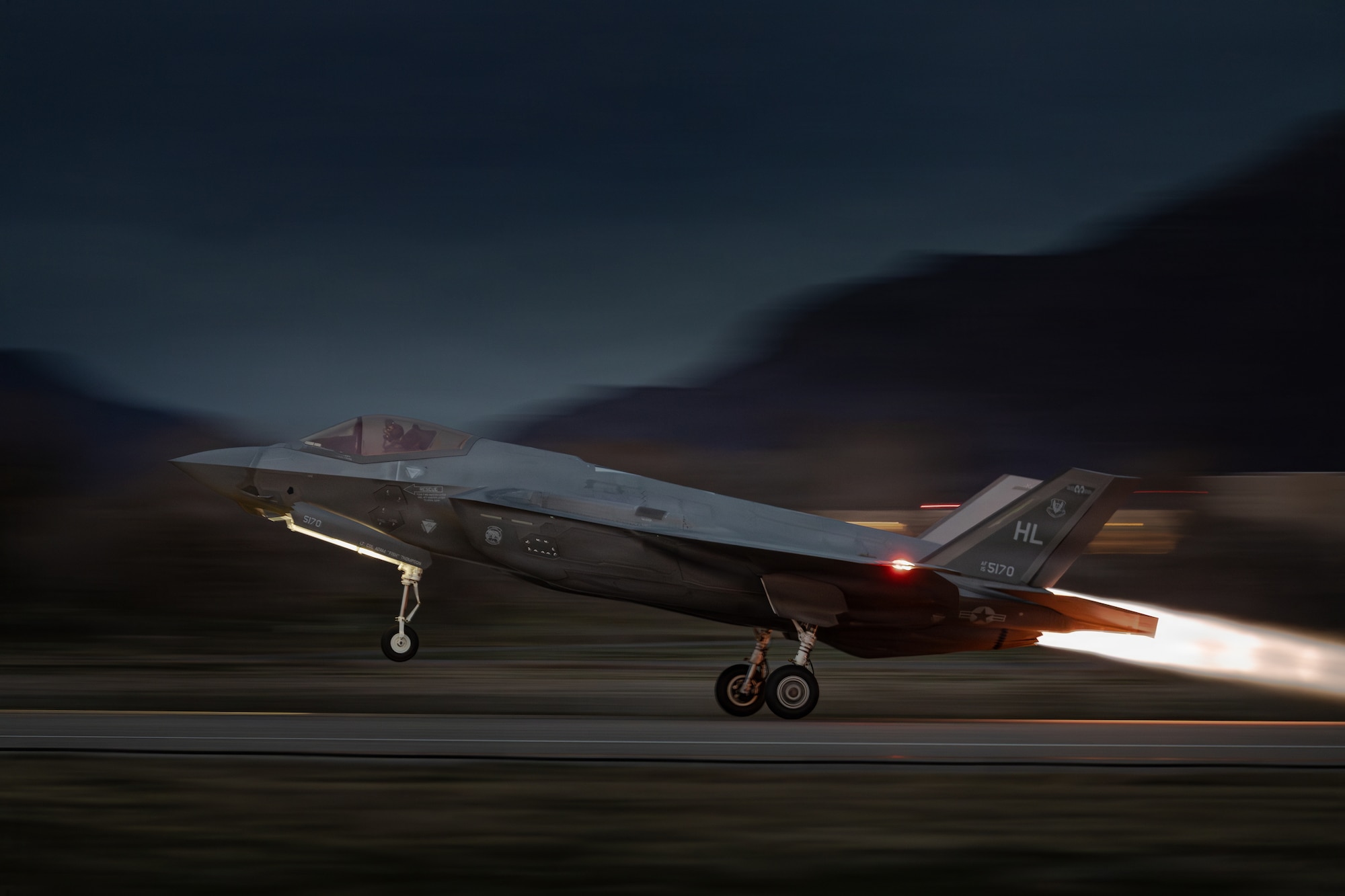 A photo of an F-35 taking off at night with afterburner and mountains in the background