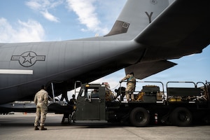 Airmen stand on a loading vehicle behind an aircraft