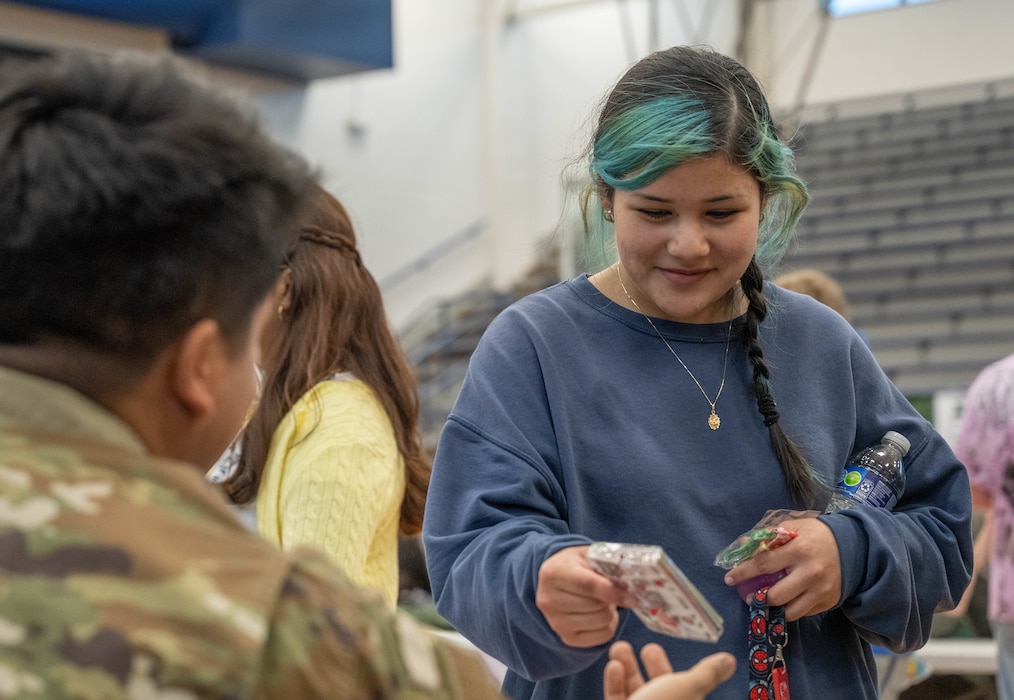 A U.S. Air Force Airman hands an object to an Altus High School student during a career fair at Altus High School, Altus, Oklahoma, March 11, 2026. Students had the opportunity to interact with Airmen from the 97th Security Forces Squadron, 97th Civil Engineer Squadron, 97th Maintenance Group, a 56th Air Refueling Squadron KC-46 Pegasus aircraft instructor pilot, and members of the Altus Sexual Assault Prevention and Response team. (U.S. Air Force photo by Airman 1st Class Emma Wright)