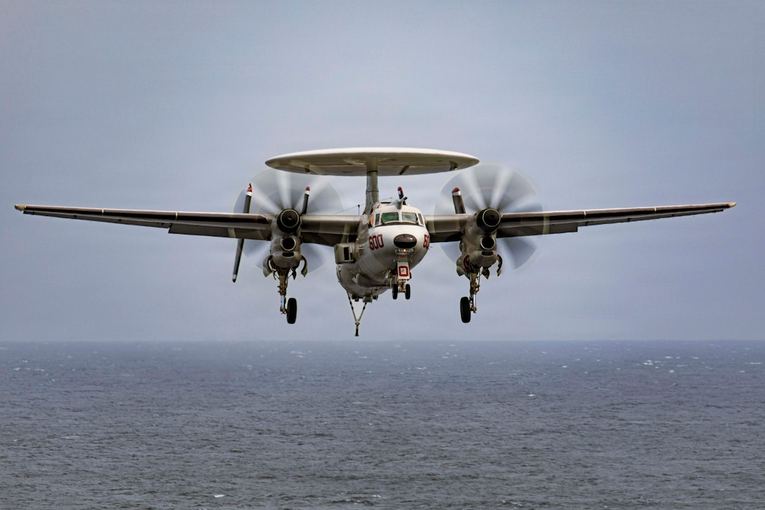 An aircraft flies in a gloomy sky over a body of water.
