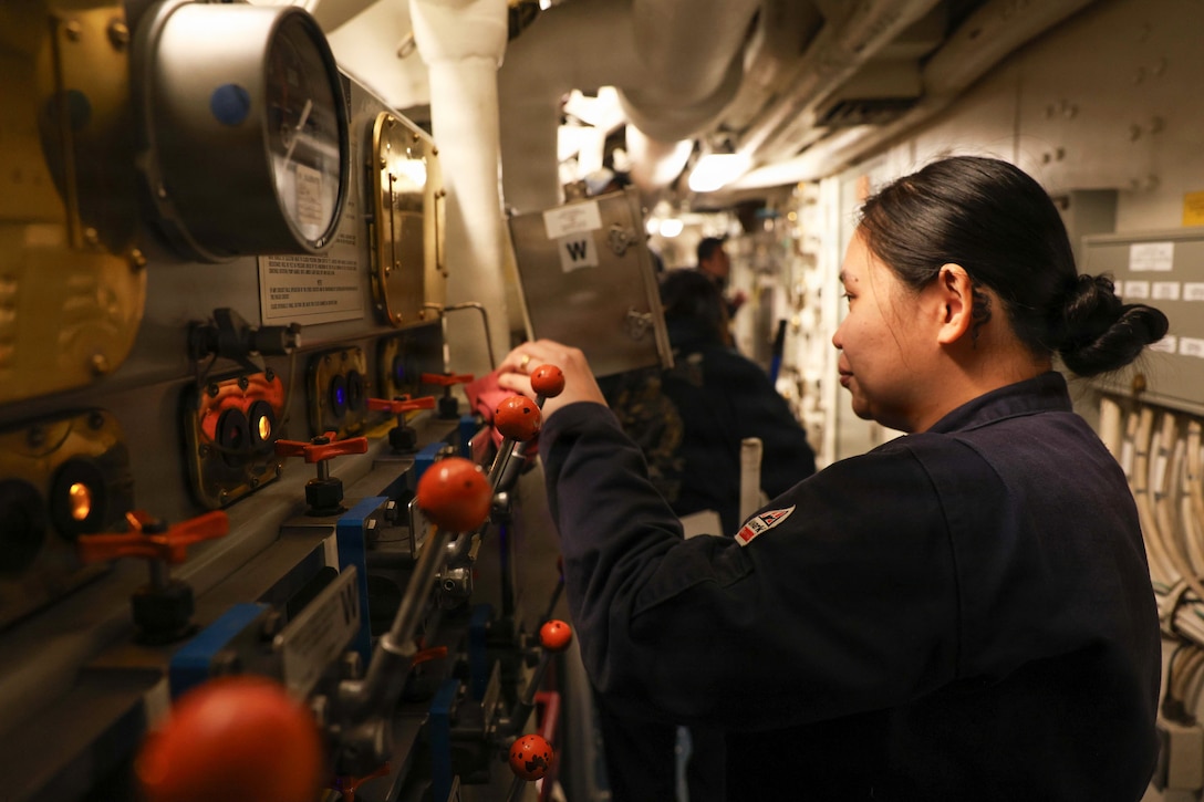 A sailor cleans a dimly lit control station aboard a ship.