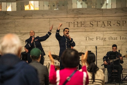 Audience members applaud as U.S. Air Force Master Sgt. Ashley Keeks, left, and Tech. Sgt. Ben Edquist, center, both vocalists with The U.S. Air Force Band’s Singing Sergeants, perform a comedic duet at the Smithsonian National Museum of American History in Washington, D.C., March 12, 2026. The Band performed two, one-hour shows for audience members as a living exhibit of American artistic contribution to culture. (U.S. Air Force photo by Staff Sgt. Jordan Powell)