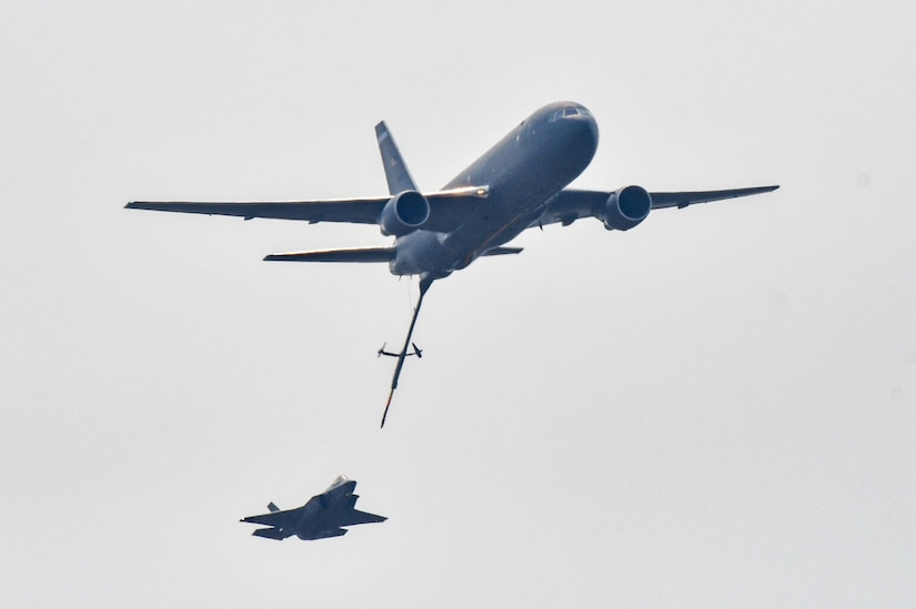 Two military aircraft fly near each other with the larger aircraft having a refueling boom extended toward the other.