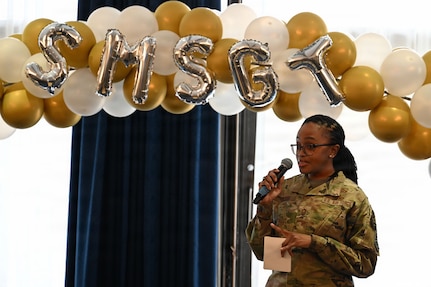 A woman speaks into a microphone in front of a window.
