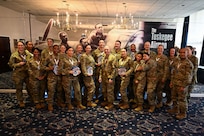 A group of 25 Airmen pose for a picture in a dimly lit ceremony room.