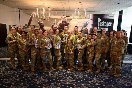 A group of 25 Airmen pose for a picture in a dimly lit ceremony room.