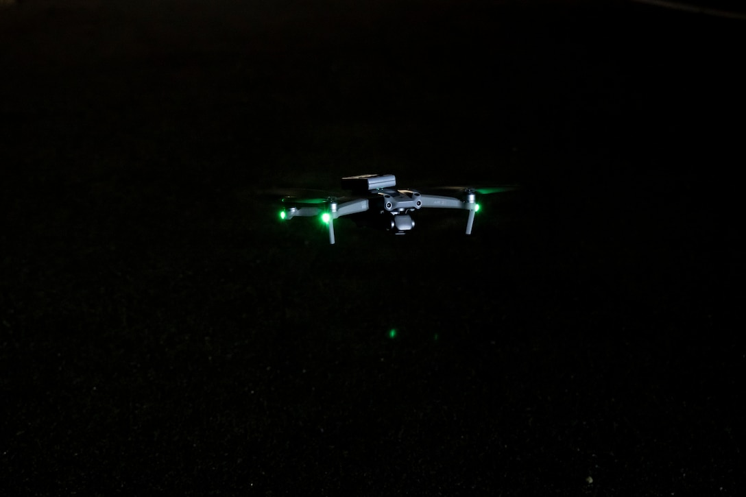 A drone with small green lights flies in dark conditions.