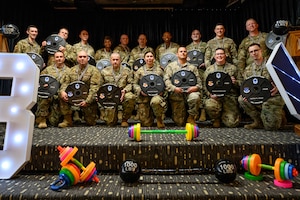 Senior master sergeant selects pose together holding a mock barbell weight labeled “The Iron Milestone,” personalized with their name, rank, unit, base, and year.