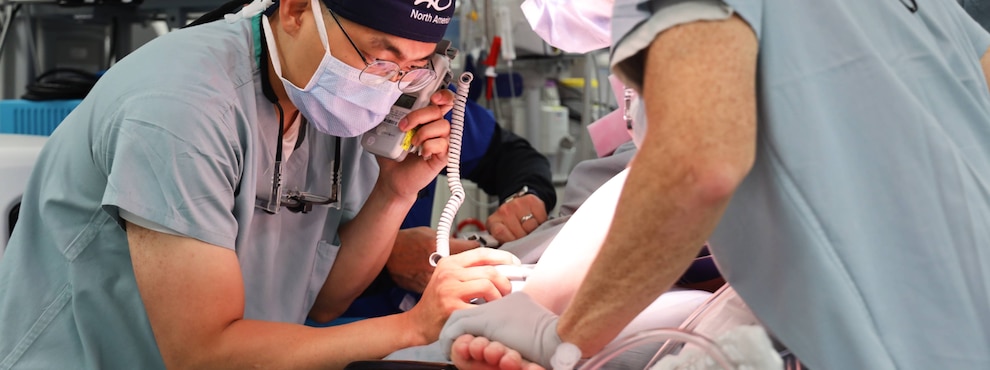 Surgeons using a dopler to prepare a surgical site on a patient's leg.