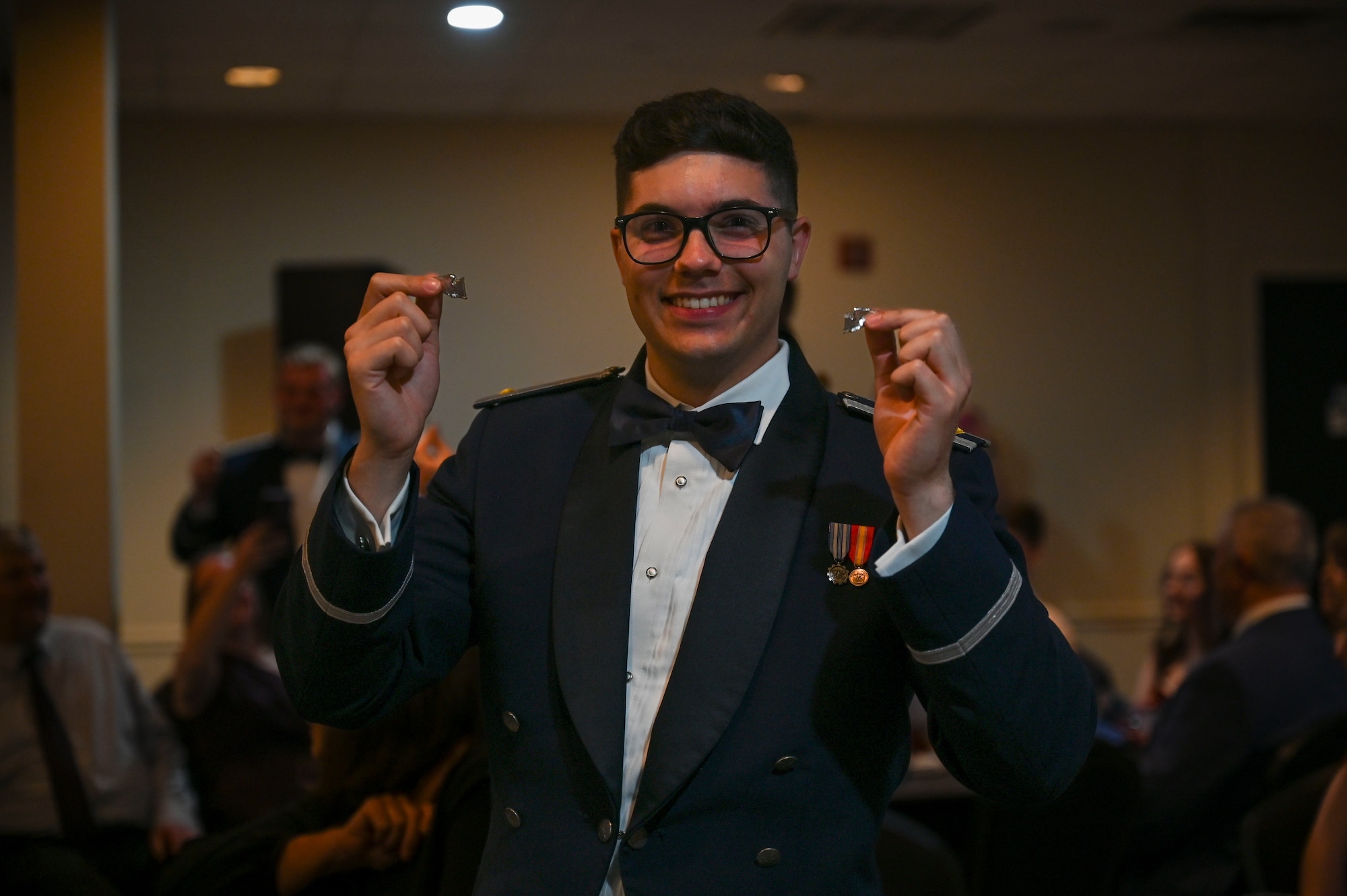 A graduating pilot holds up his broken silver wings.