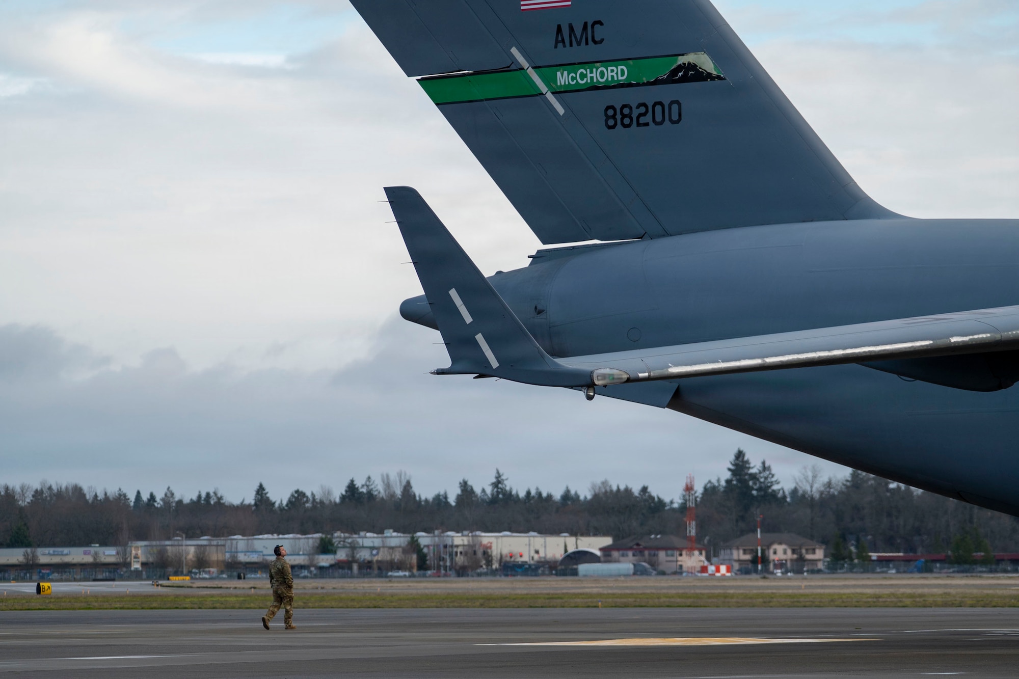 A U.S. Air Force airman walks on a flightline next to U.S. Air Force cargo plane from the back. The tail of the plane has "McChord' written on it.