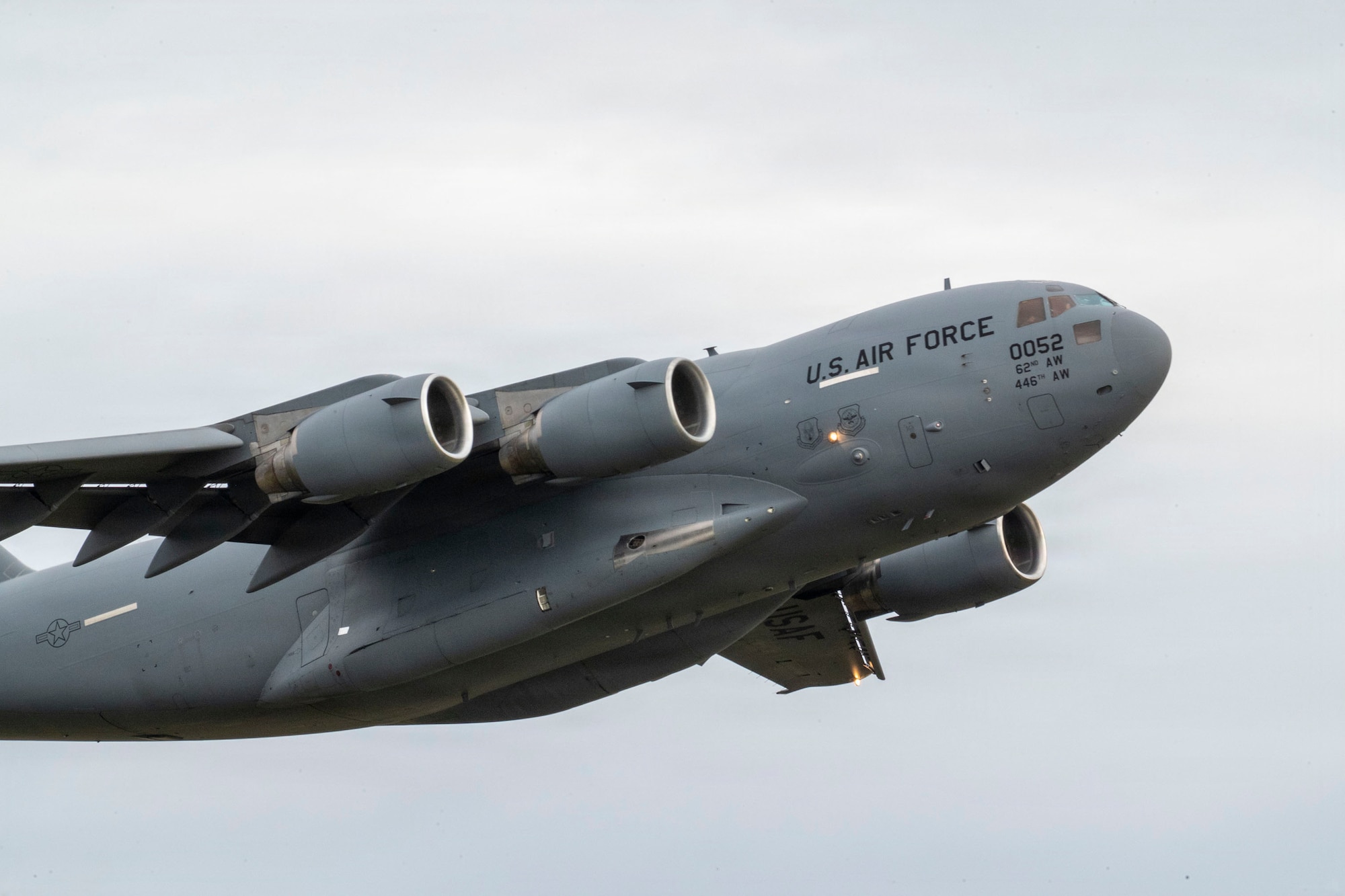 A U.S. Air Force cargo plane mid-flight with a background of grey clouds