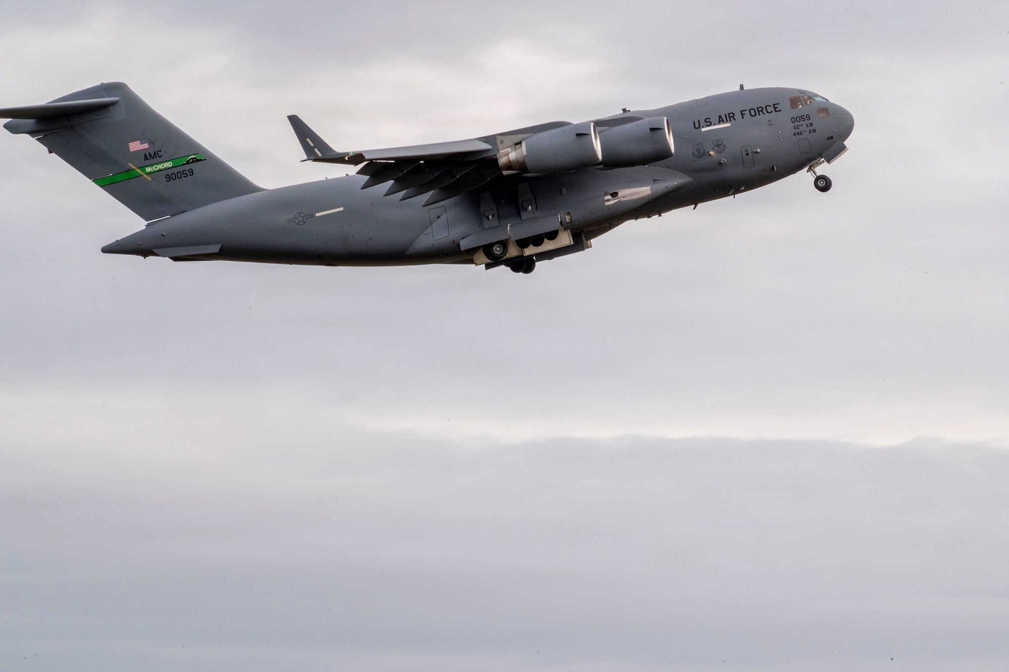 A U.S. Air Force cargo plane taken from the side of the aircraft mid-flight with a background of grey clouds