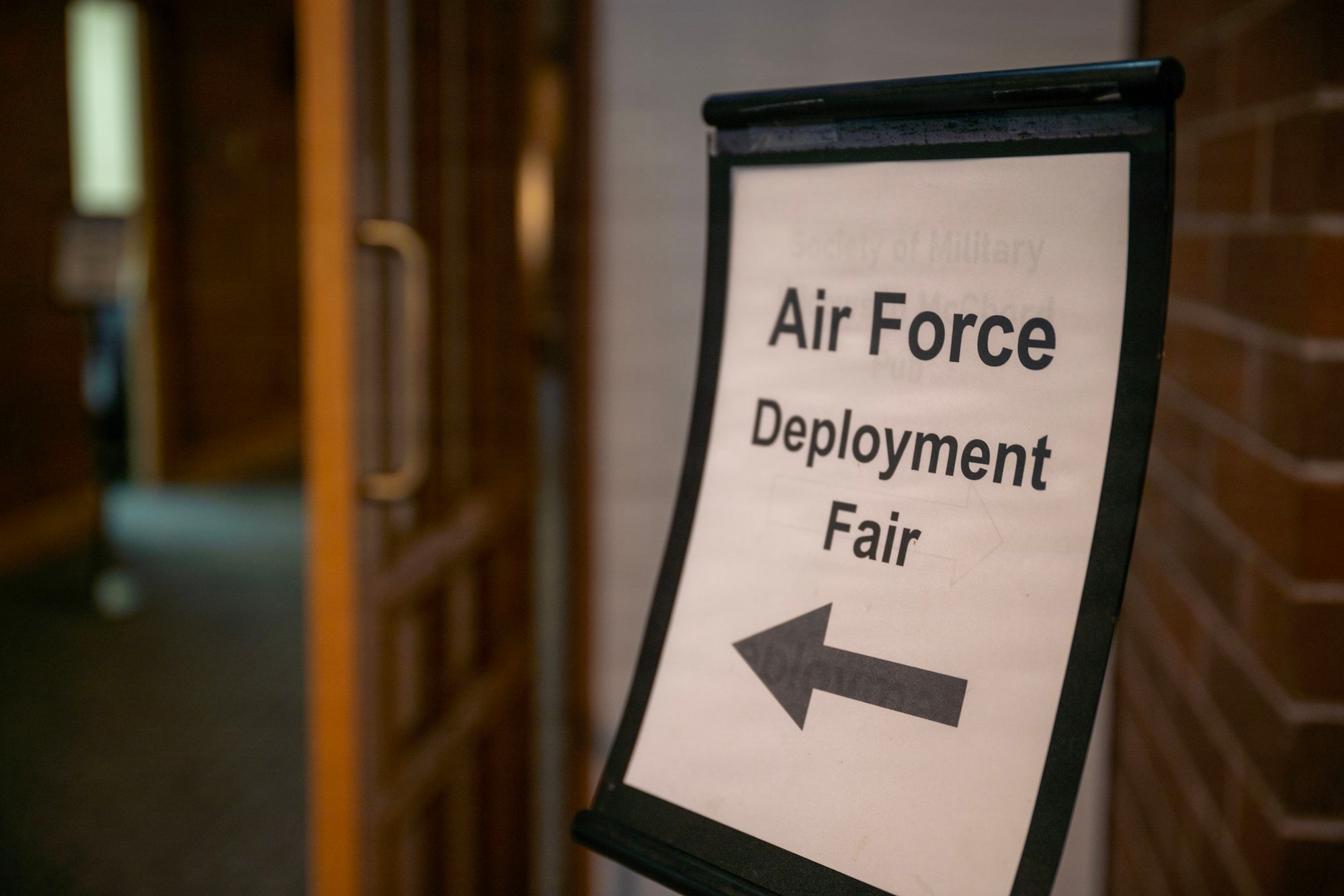 A sign displaying the text "Air Force Deployment Fair" with an arrow pointing to the left. To the left of the photograph is an open doorway.