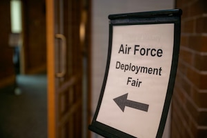 A sign displaying the text "Air Force Deployment Fair" with an arrow pointing to the left. To the left of the photograph is an open doorway.