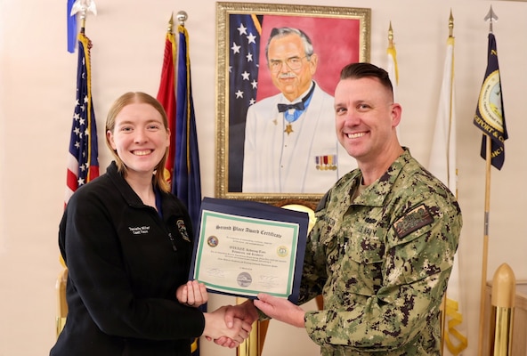 Hospital Corpsman 3rd Class Kaitlyn D. Miller (left) receives a second-place award from Cmdr. William “Bill” Lawson (right), interim executive officer, during the command process improvement fair at Navy Medicine Readiness and Training Command Twentynine Palms, March 13, 2026. Miller led the Wide Awake Local Anesthesia No Tourniquet (WALANT): Reducing Time, Resources, and Recovery project, which improved efficiency and reduced patient hospital time. (U.S. Navy photo by Christopher Jones, NMRTC / Naval Hospital Twentynine Palms public affairs officer).