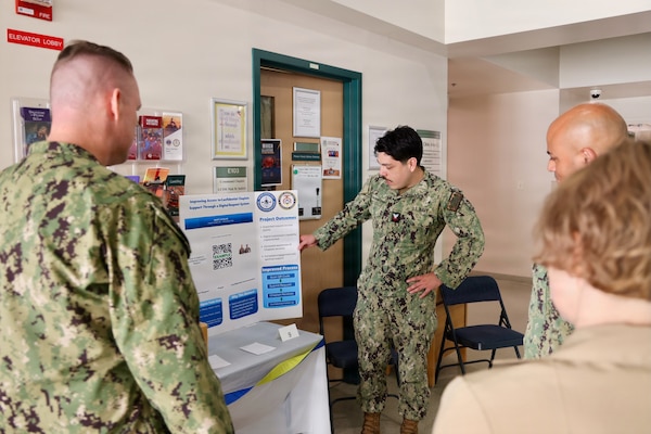 Religious Personnel Specialist 2nd Class Diego Escalante shares his process improvement project with Cmdr. William “Bill” Lawson (left), interim executive officer, and Command Master Chief Richard Moreno (right) during the command process improvement fair at Navy Medicine Readiness and Training Command Twentynine Palms, March 13, 2026. (U.S. Navy photo by Christopher Jones, NMRTC / Naval Hospital Twentynine Palms public affairs officer).