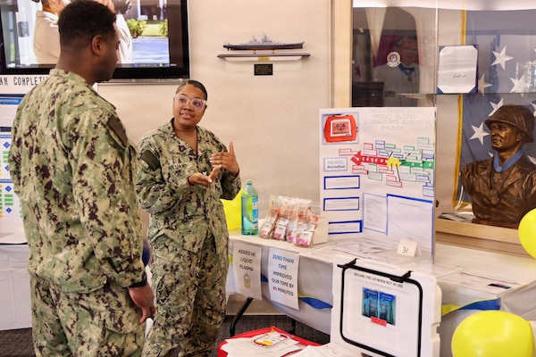 Hospital Corpsman 1st Class Meosha Williams (right) presents her process improvement project to Lt. Cmdr. Kino Anderson (left) during the command process improvement fair at Navy Medicine Readiness and Training Command Twentynine Palms, March 13, 2026. (U.S. Navy photo by Christopher Jones, NMRTC / Naval Hospital Twentynine Palms public affairs officer).