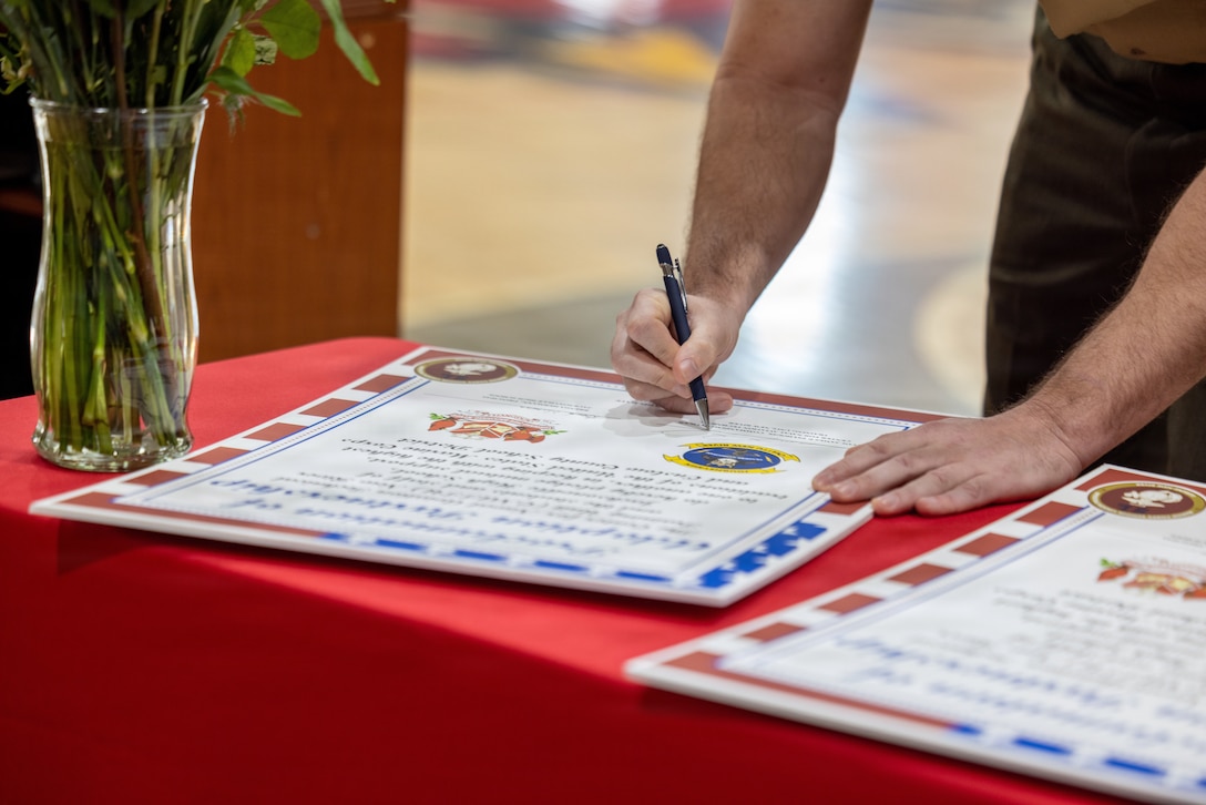 U.S. Marine Corps Lt. Col. James P. Psyhogis, commanding officer, Center for Naval Aviation Technical Training Unit New River, signs the adoption proclamation during an Adopt-a-School ceremony at Jacksonville High School in Jacksonville, North Carolina, March 18, 2026. The final adoption ceremony between Jacksonville High School and the Center for Naval Aviation Technical Training Unit New River marked a significant achievement for Onslow County School District as it reached a 100 percent adoption rate by various units of Marine Corps Installations East and II Marine Expeditionary Force in the Adopt-a-School program. This initiative aims to strengthen the bond between the military and the local community. (U.S. Marine Corps photo by Lance Cpl. Alyssa J. DeCrane)