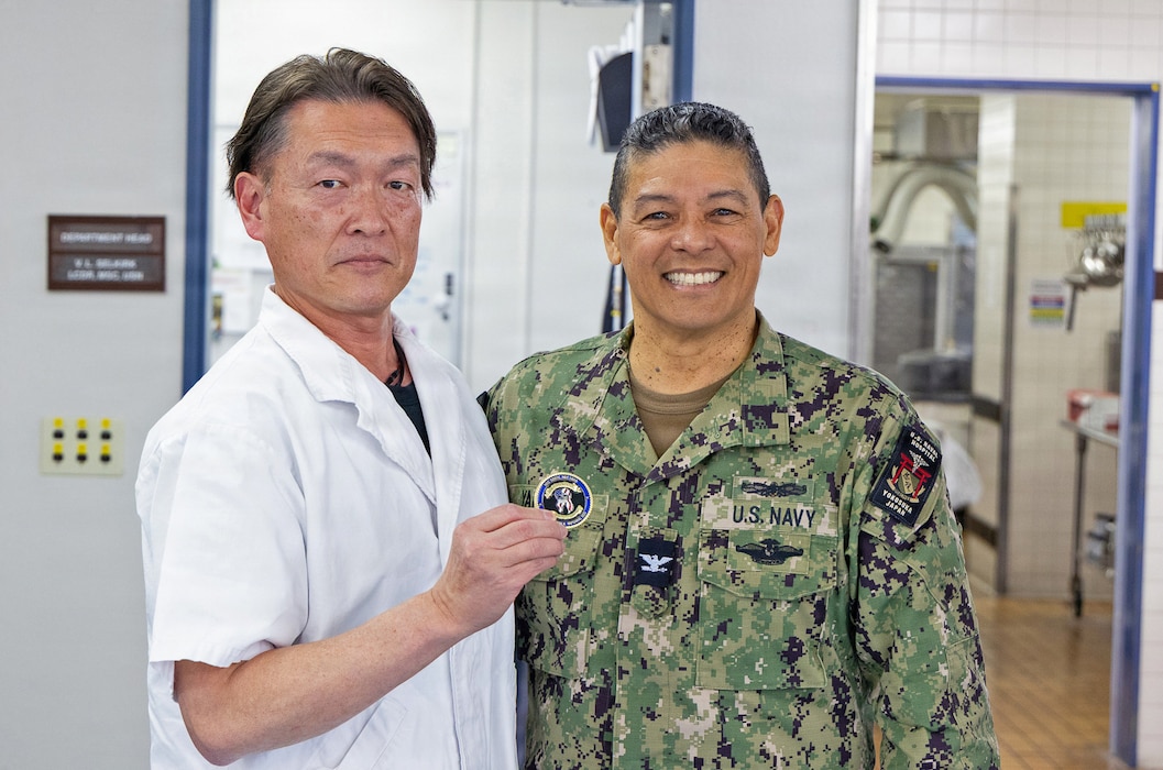 YOKOSUKA, Japan (March 16, 2026) – Mr. Katsuo Konno, a master labor contract employee and galley supervisor at U.S. Naval Hospital Yokosuka, receives a personal coin from Capt. Donavon YapShing, the hospital’s deputy director, during a recognition ceremony at the hospital. Konno was honored for his exemplary service, leadership and commitment to supporting hospital operations and patient care. U.S. Naval Hospital Yokosuka ensures warfighter readiness and delivers high-quality health care to forward-deployed forces and their families. (U.S. Navy photo by Daniel Taylor/USNMRTC Yokosuka Public Affairs)