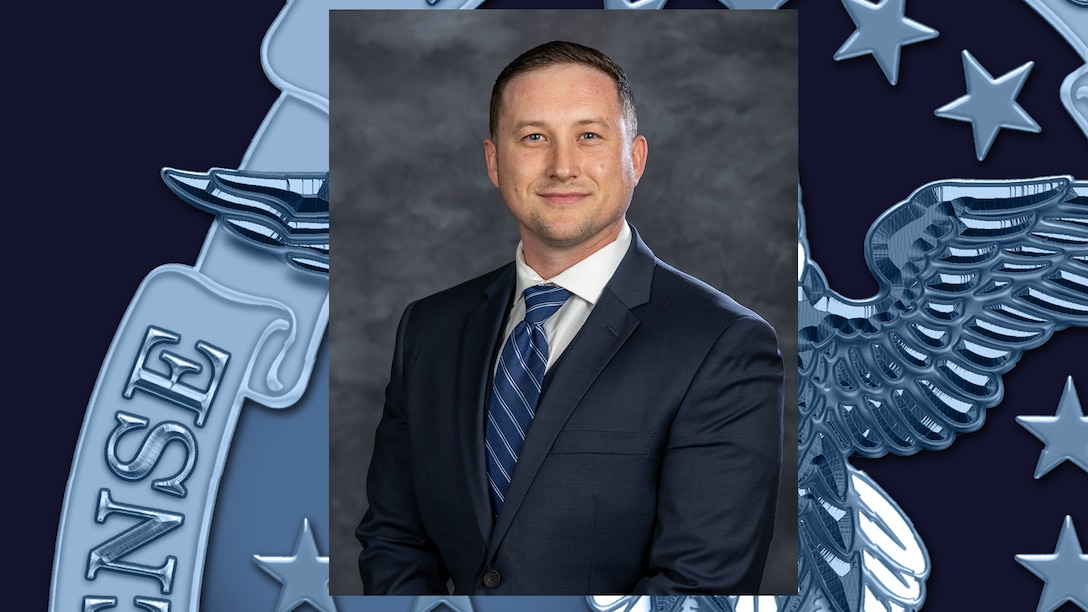 Headshot of man in dark navy suit, white shirt and blue diagonal -striped tie