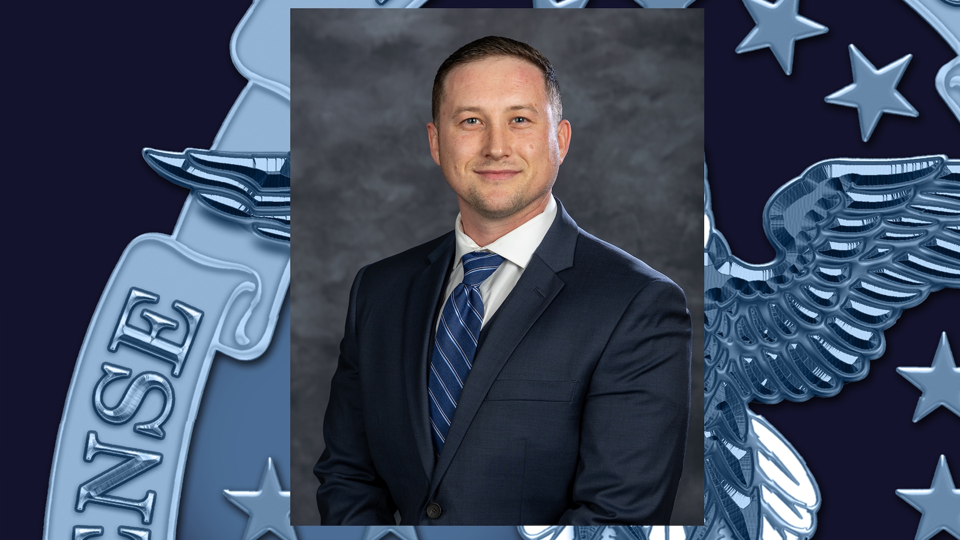 Headshot of man in dark navy suit, white shirt and blue diagonal -striped tie