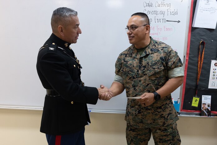 U.S. Marine Corps Col. Ernest Govea, commanding officer, Marine Corps Base Camp Blaz, presents retired Sgt. Maj. Vincent Santiago, an invitation to the 249th Marine Corps Ball while visiting Okkodo High School in Dededo, Guam, Oct. 23, 2024. MCB Camp Blaz leadership visited Okkodo High School to invite the JROTC leadership to the 249th Marine Corps Birthday, and to show appreciation to the JROTC leadership and students for their continued support to the Marines and Sailors at MCB Camp Blaz. (U.S. Marine Corps photo by Lance Cpl. Tanner Currin)