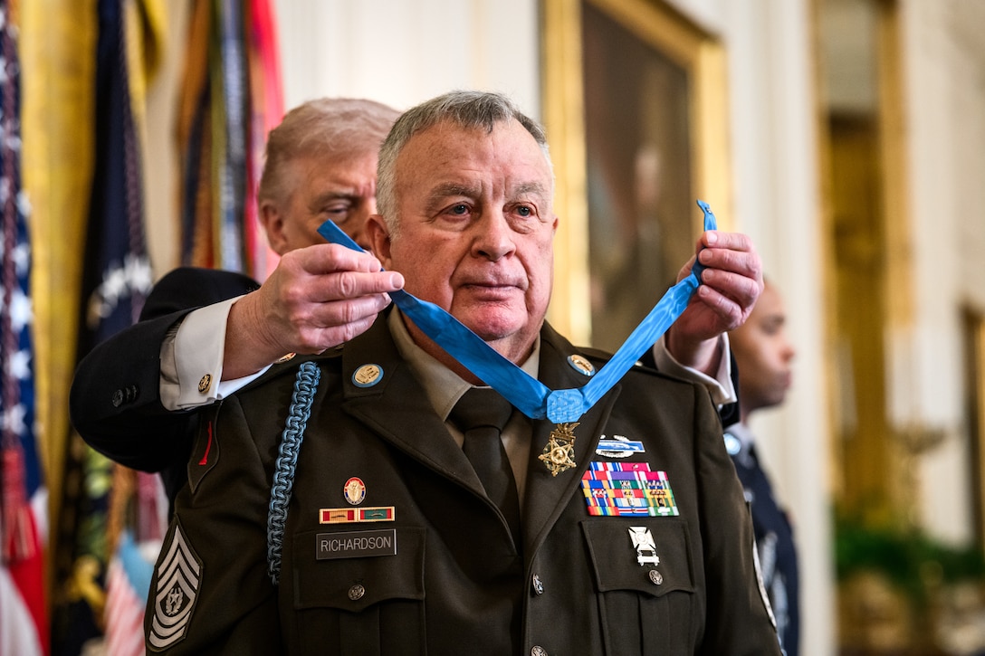 A veteran in Army uniform stands in front of President Donald J. Trump, who places a medal on a ribbon around the veteran's neck.