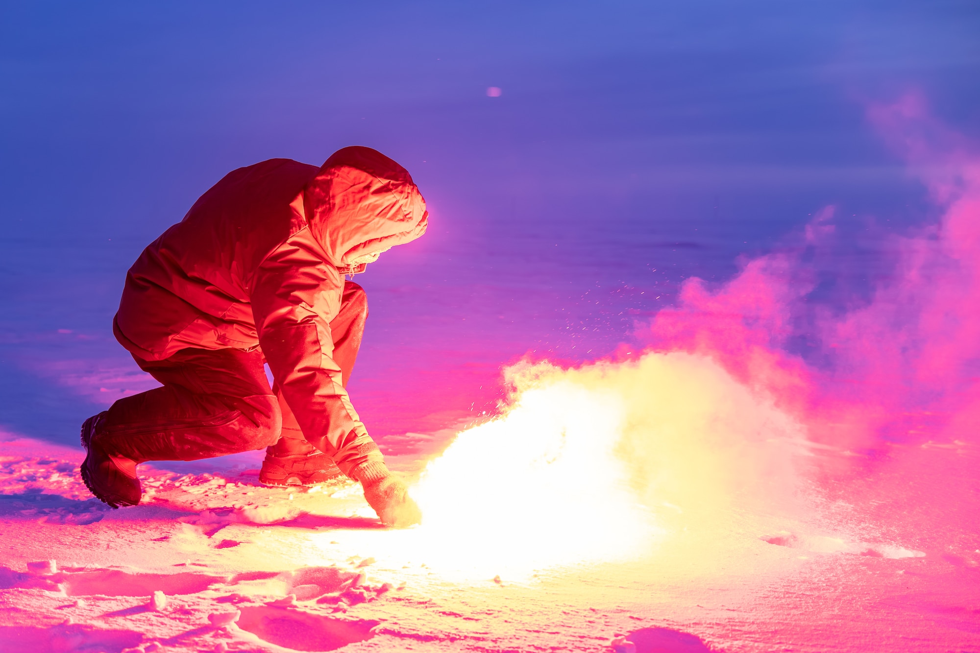 A man kneels while lighting a flare on the frozen tundra.