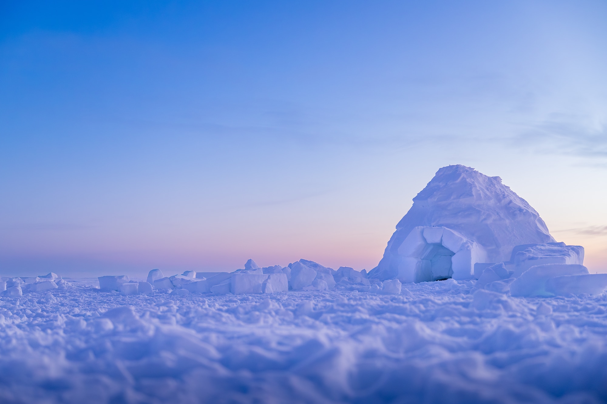 An igloo sits on a frozen tundra during a sunset.
