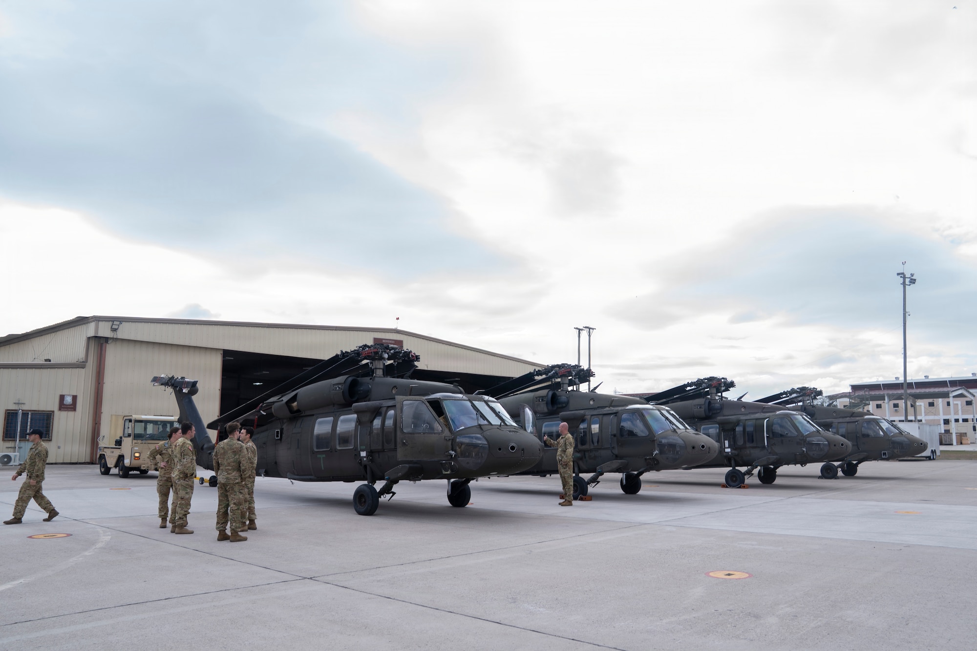 four military helicopters in a line and people wearing military uniforms walking around