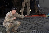 A military member stands on a military plane and guides a helicopter.