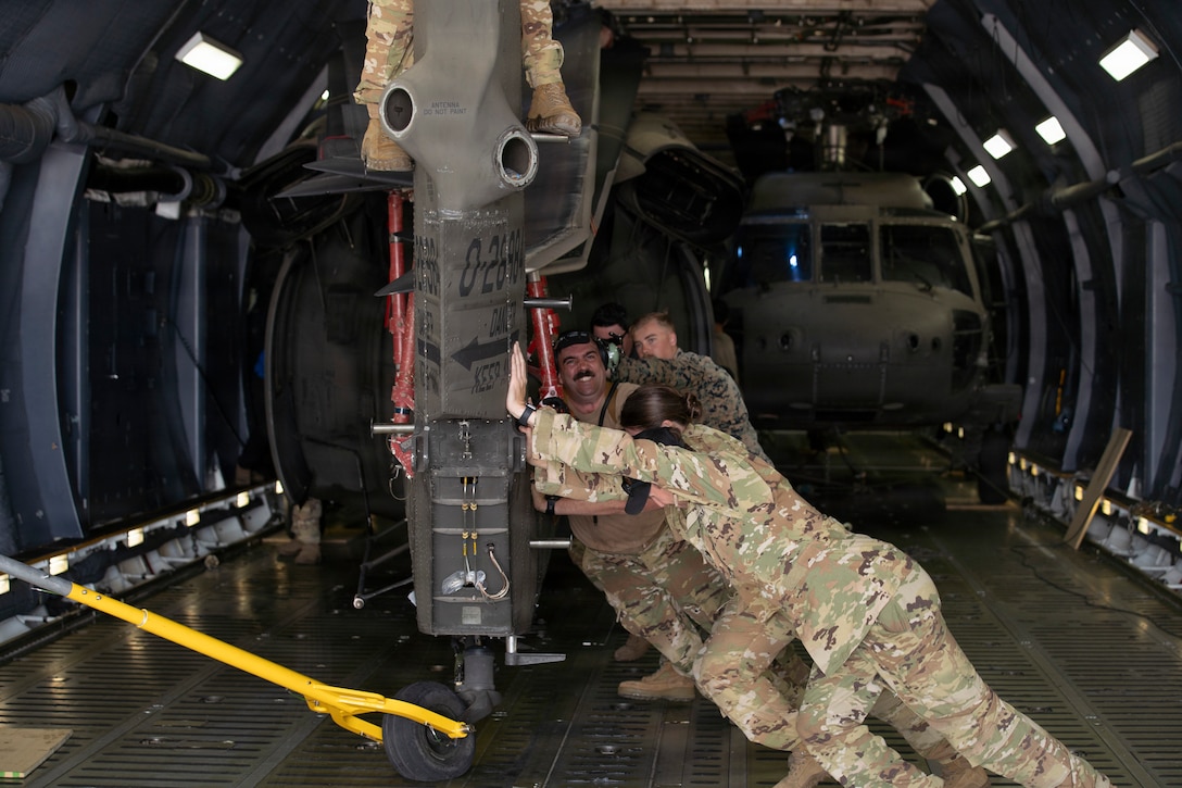 Military members push a helicopter onto a military plane.