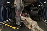 Military members push a helicopter onto a military plane.