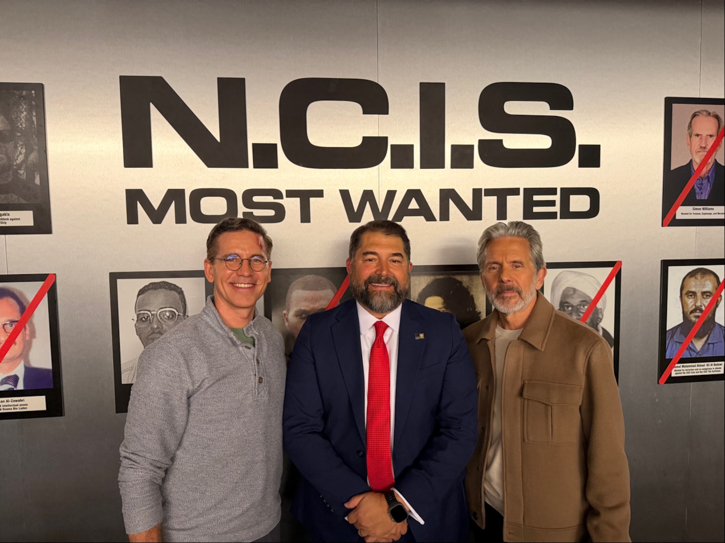 Naval Criminal Investigative Service Director Omar Lopez stands with cast members from CBS' NCIS television series in front of the infamous Most Wanted wall from the show.