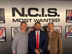 Naval Criminal Investigative Service Director Omar Lopez stands with cast members from CBS' NCIS television series in front of the infamous Most Wanted wall from the show.