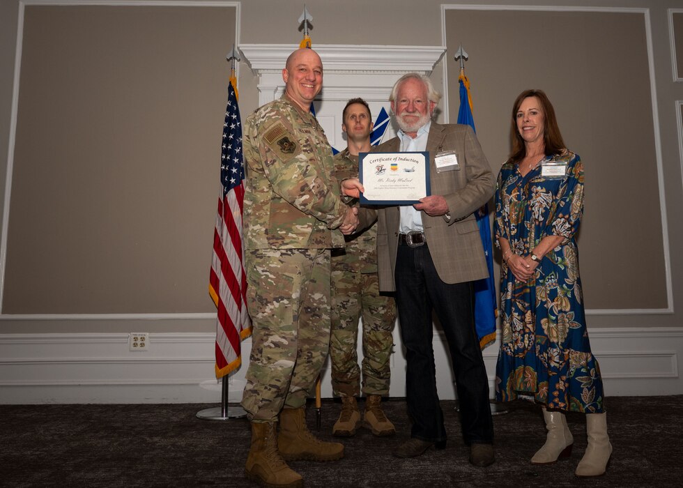 Service member and Honorary Commander shake hands while holding a certificate.