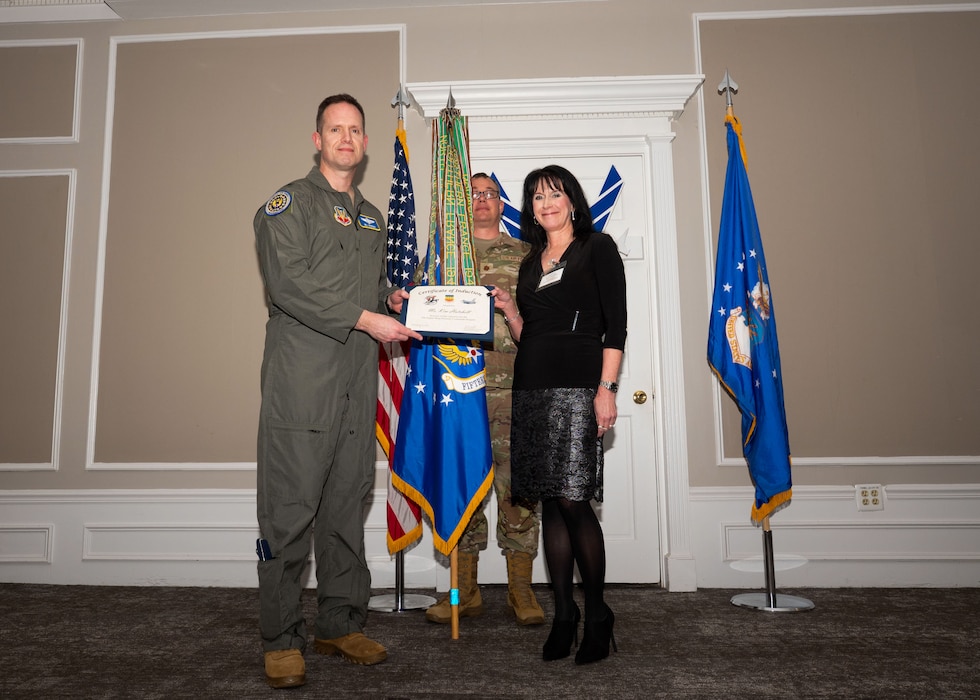 Service member and Honorary Commander shake hands while holding a certificate.
