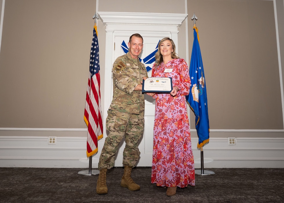 Service member and Honorary Commander shake hands while holding a certificate.
