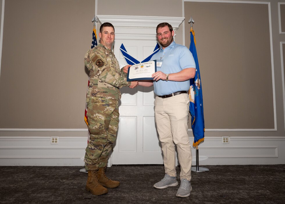Service member and Honorary Commander shake hands while holding a certificate.