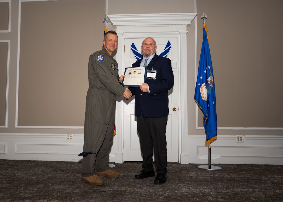 Service member and Honorary Commander shake hands while holding a certificate.