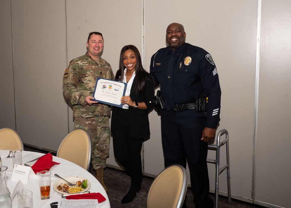 Service member and Honorary Commander shake hands while holding a certificate.