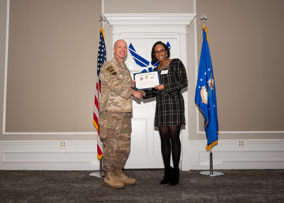 Service member and Honorary Commander shake hands while holding a certificate.