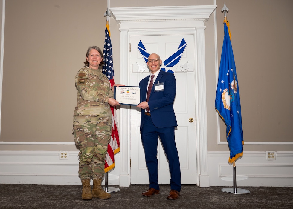 Service member and Honorary Commander shake hands while holding a certificate.