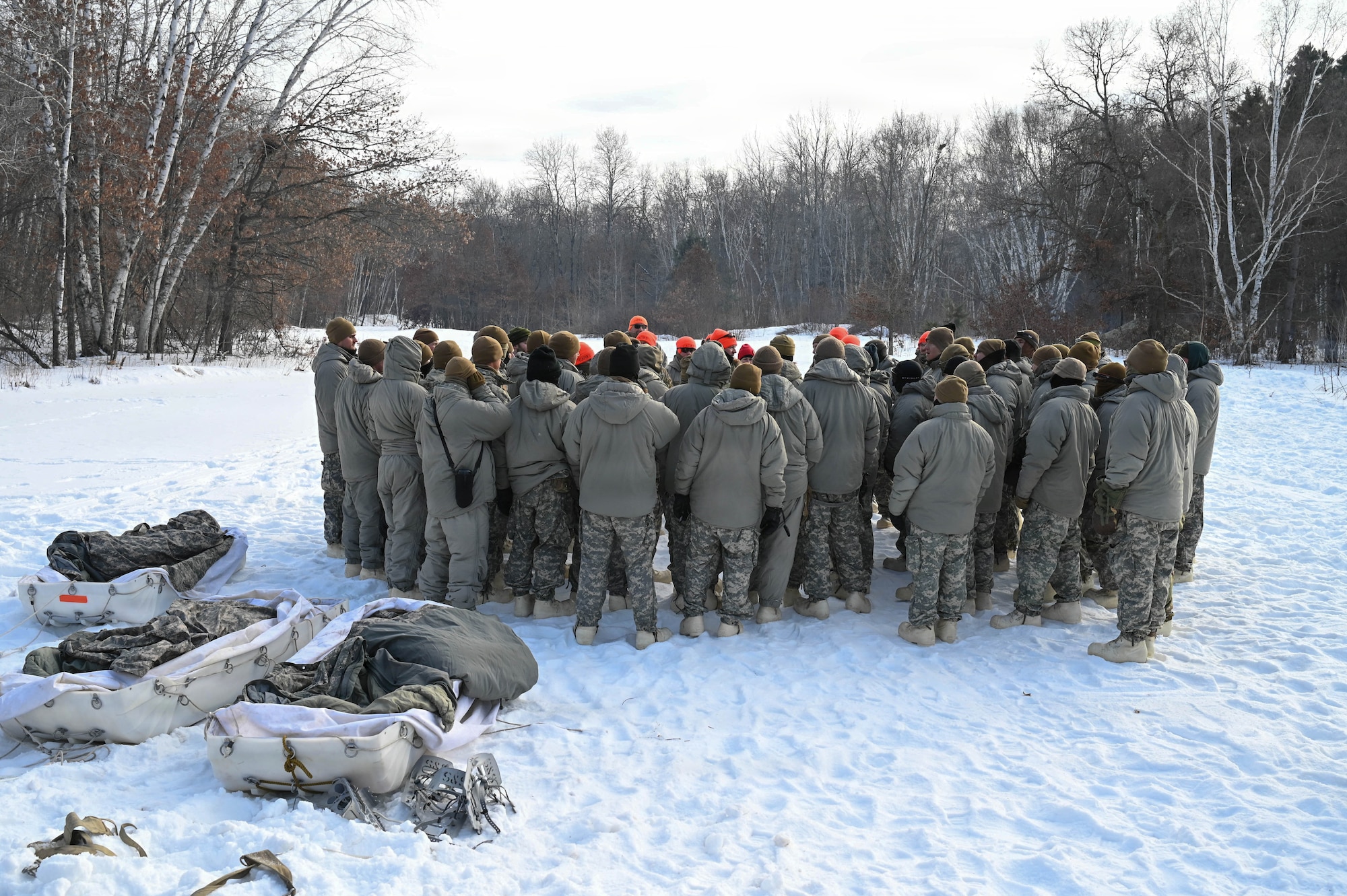 Cold weather course participants stand in a circle around cadre and talk about the training.