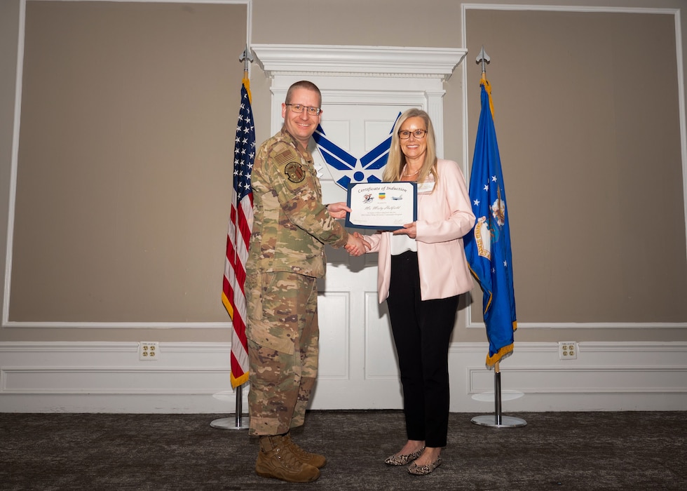 Service member and Honorary Commander shake hands while holding a certificate.