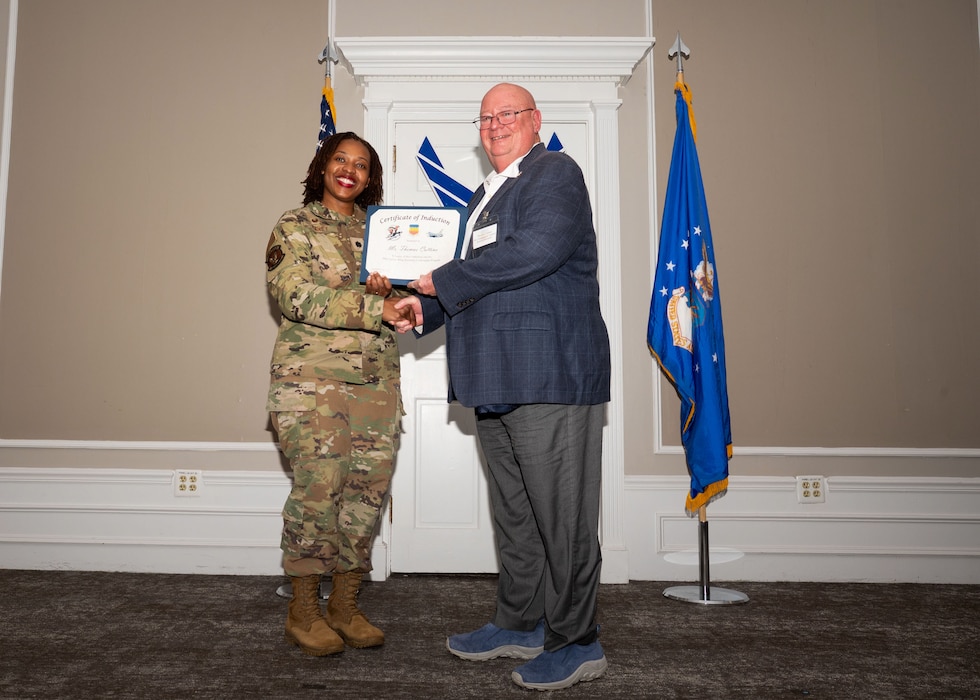 Service member and Honorary Commander shake hands while holding a certificate.
