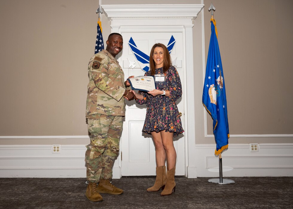 Service member and Honorary Commander shake hands while holding a certificate.