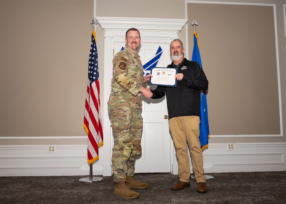 Service member and Honorary Commander shake hands while holding a certificate.